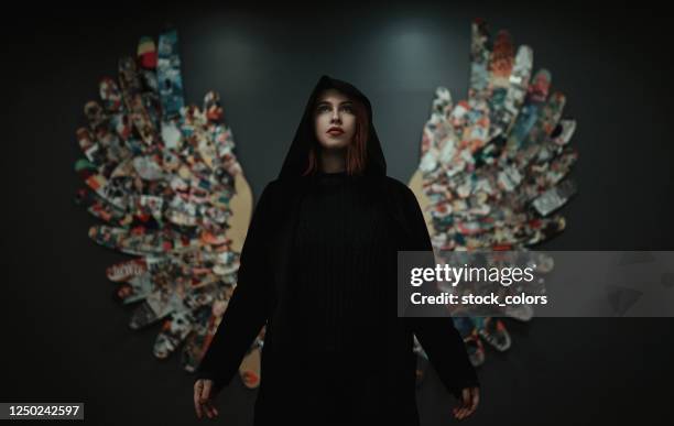 redhead woman with dark clothes posing with wings on the wall... - devil woman stock pictures, royalty-free photos & images