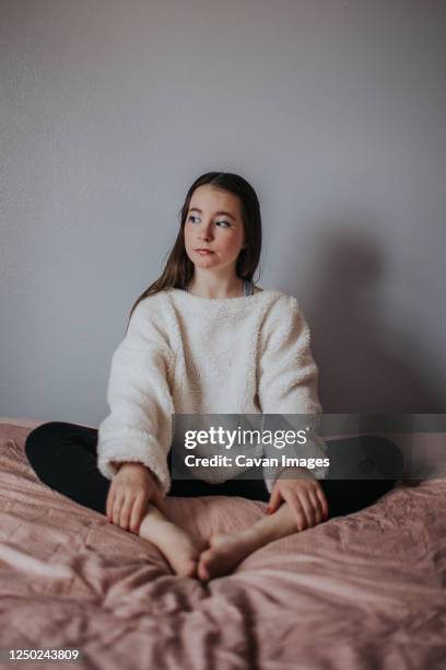 vertical portrait of tween girl sitting on bed looking away - family photo shoot stock pictures, royalty-free photos & images