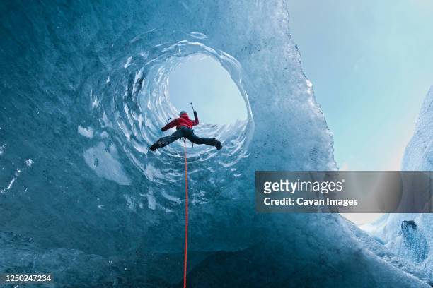 woman climbing out of glacier cave / s√≥lheimaj√∂kull glacier in iceland - s the adventures of rin tin tin stockfoto's en -beelden