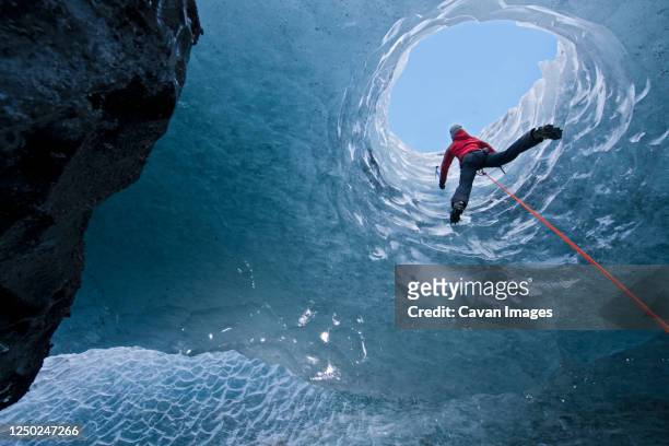 woman climbing out of glacier cave / s√≥lheimaj√∂kull glacier in iceland - ice climbing stockfoto's en -beelden