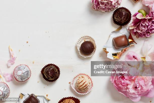 still life of open chocolates and wrappers with flowers - candy wrapper stock pictures, royalty-free photos & images