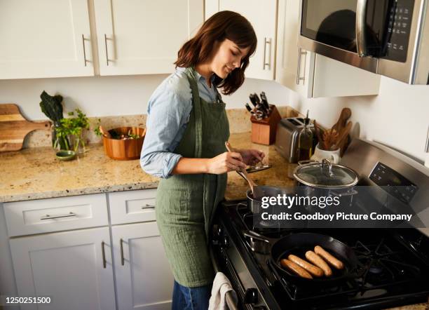 smiling young woman preparing a meal on her stove - stir frying european stock pictures, royalty-free photos & images