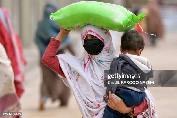 Woman carries her child while she leaves with a free bag of flour from a government distribution point in Islamabad on April 1, 2023. - At least 11...