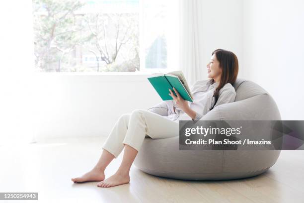 woman reading a book on sofa - ビーズソファ ストックフォトと画像