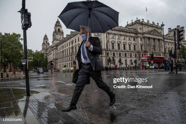 Man jumps over a puddle in Parliament Square during a thunderstorm on June 17, 2020 in London, England.