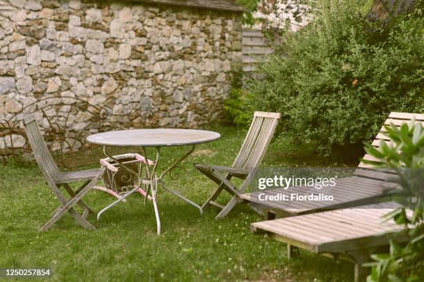 the back yard of a private house with a green lawn, wooden old sun loungers, chairs and a round table - stone wall garden stock pictures, royalty-free photos & images