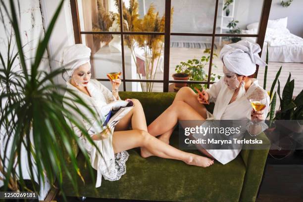 two girlfriends in bathrobes and face masks are sitting on the couch. - picture magazine stockfoto's en -beelden