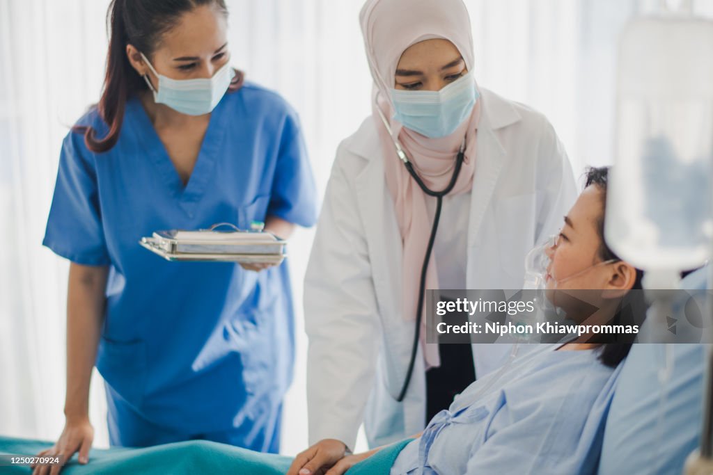 Young Asian woman Muslim doctor and nurse giving advice discussion and check up to elderly patient sitting in bed at hospital which smiling and felling happy. Medicine and health care safe concept.