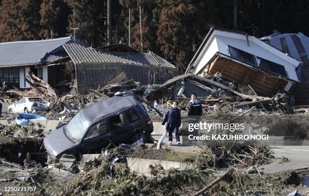 Pedestrians stand next to collapsed houses after being hit by a tsunami in Minamisoma, Fukushima Prefecture on March 12, 2011. More than 1,000 people...