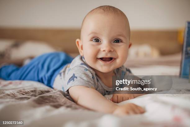 schöne baby junge auf dem bett liegen und lächelnd - männliches baby stock-fotos und bilder