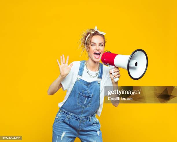 junge frau in dungarees schreien in megafon - jeans latzhose frau stock-fotos und bilder