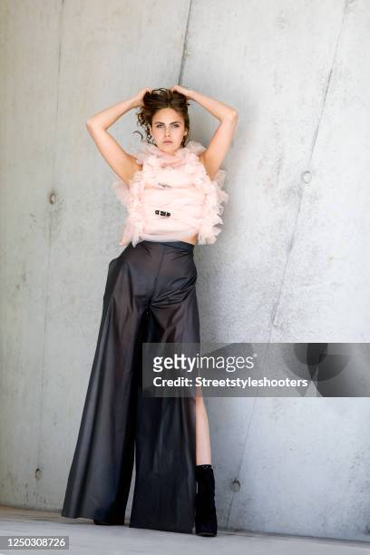 Model and influencer Elena Carriere wearing a rose colored bustier with black buckles and dark grey foil fabric pants with open sides by Marina...