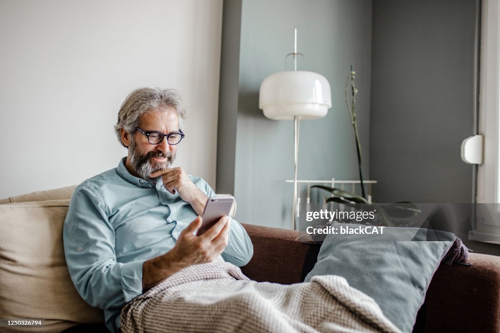 De rijpe mens gebruikt mobiele telefoon thuis