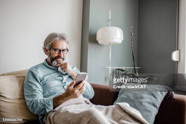 mature man is using mobile phone at home - mature men imagens e fotografias de stock