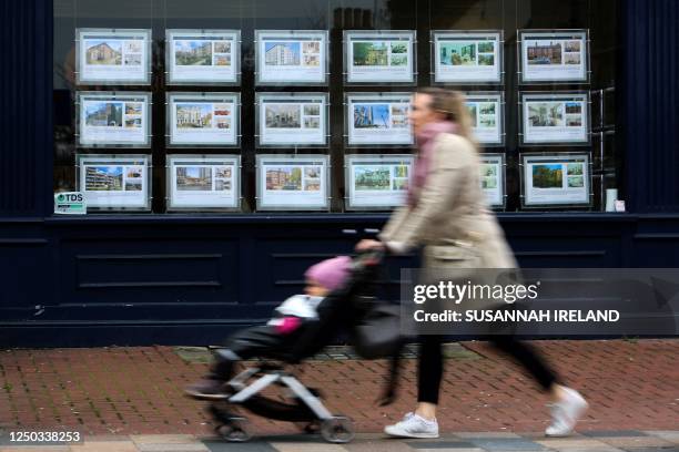 Pedestrians walk past the front window of an estate agent advertising properties to let and to sell in Lavender Hill, in South London, on April 1,...