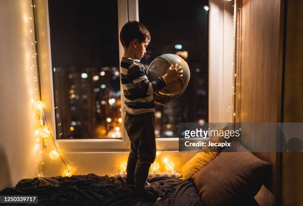 netter junge hält globus in den händen und träumt von reisen während coronavirus haus isolation - child globe stock-fotos und bilder