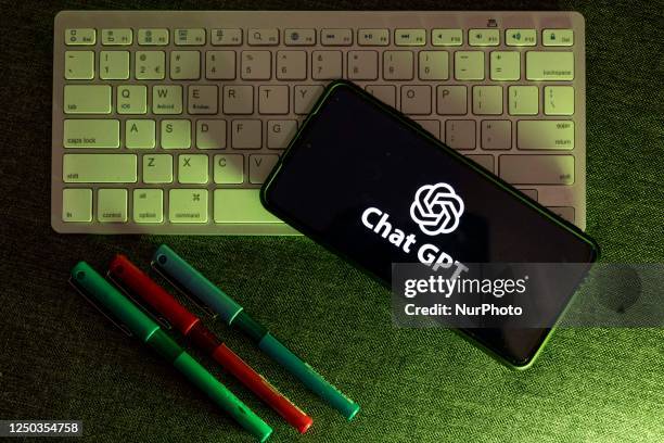 Photo illustration showing ChatGPT and OpenAI research laboratory logo and inscription at a mobile phone smartphone screen on a keyboard. Open AI is...