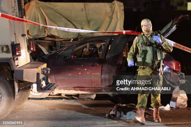 An Israeli soldier stands in front of a damaged vehicle at the site of a ramming attack near the town of Beit Ummar, north of Hebron city in the...