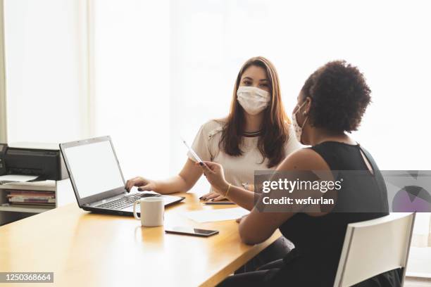 two young women talking in an office wearing a protective face mask. - employee engagement mask stock pictures, royalty-free photos & images