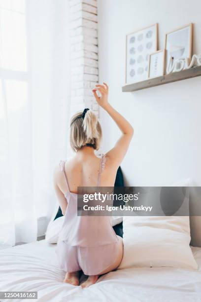 rear view of young blond woman sitting on bed - woman back pillow blonde stock pictures, royalty-free photos & images