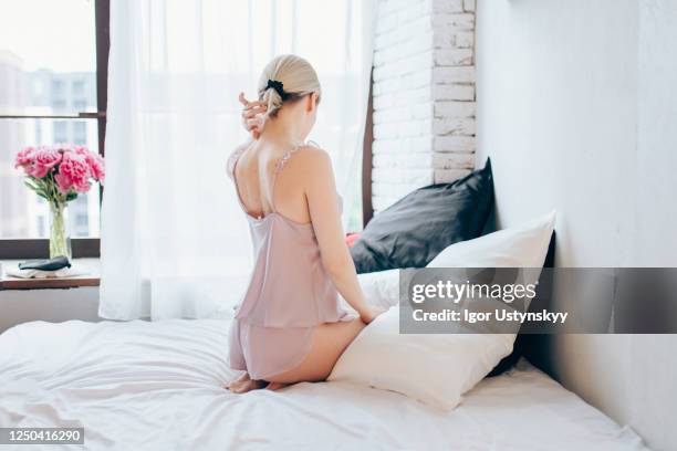 rear view of young blond woman sitting on bed - woman back pillow blonde stock pictures, royalty-free photos & images