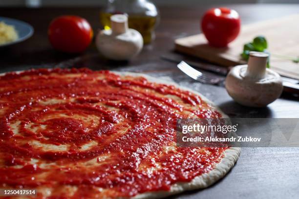 cooking italian vegetarian pizza with vegetables and mushrooms at home, on a wooden table. ketchup is smeared on the dough. step-by-step instructions, do it yourself. step 3. - tomato paste stock pictures, royalty-free photos & images