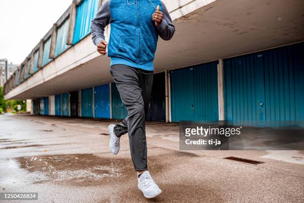 young man running over the puddle by the garages - jogging stock pictures, royalty-free photos & images
