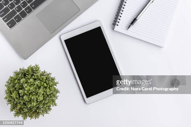 modern digital tablet on top of office desk with laptop, note pad, pen and potted green plant - laptop on desk mockup stock pictures, royalty-free photos & images