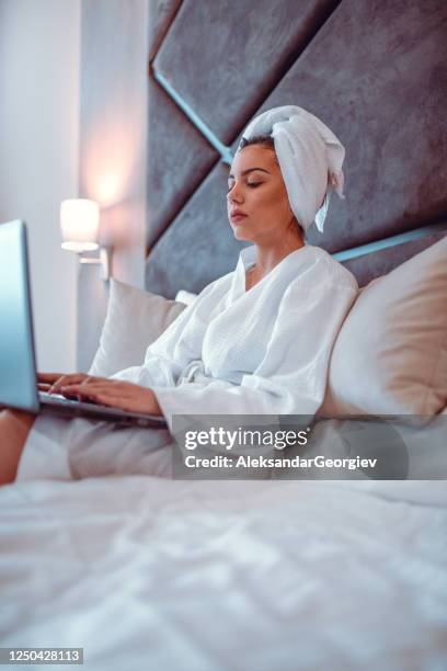 wijfje in bad robe het ontspannen op bed met laptop - bath robe stockfoto's en -beelden