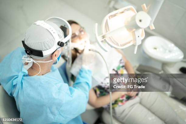 dentiste aîné examinant les dents d’une jeune femme - dentist office photos et images de collection