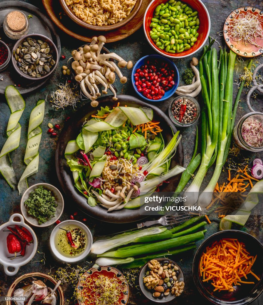 Healthy vegan lunch bowl making. Detox beautiful Buddha bowl with various fresh vegetables, edamame beans, mushrooms, seasoning and pumpkin seeds and nuts topping