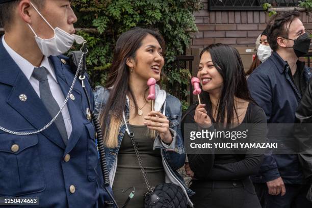 People eat phallic-shaped lollipops as a police officer stands guard during the Kanamara festival in Kawasaki on April 2, 2023.