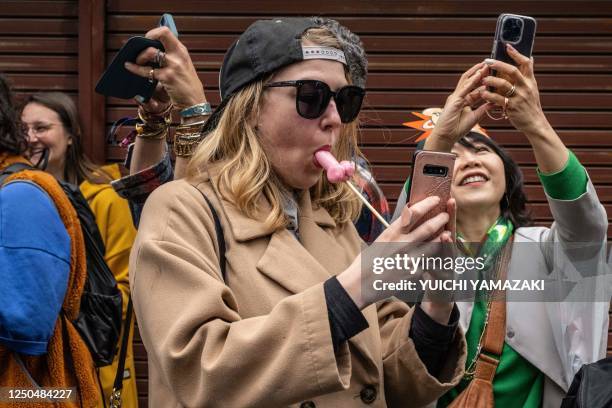 Woman eating phallic-shaped lollipop takes photographs of a parade during Kanamara festival in Kawasaki on April 2, 2023.