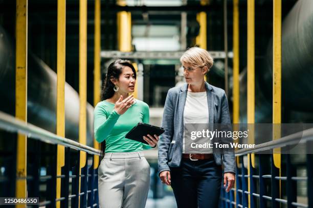 two women discussing work among large machinery - entrepreneur manufacturing stock pictures, royalty-free photos & images