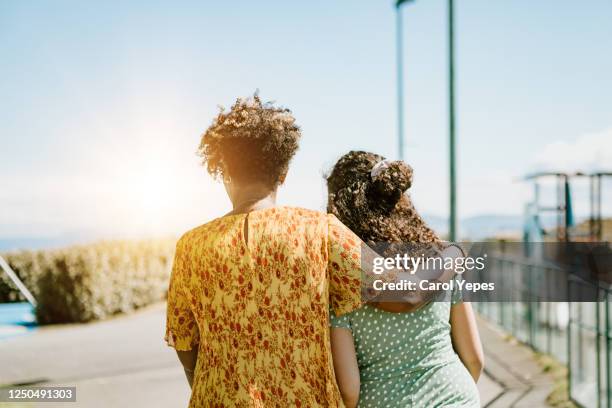 rear view of afro-american mother and daughter embracing in public park - adolescent daughter mother portrait stock-fotos und bilder