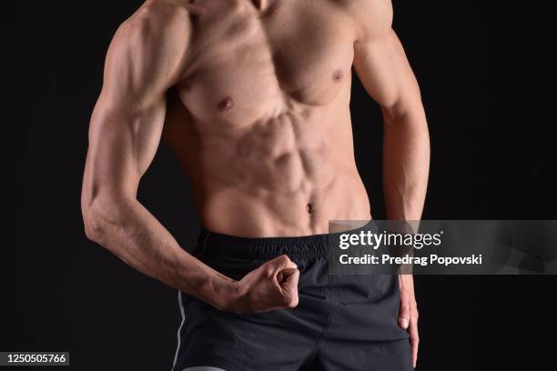 young man showing his bicep, chest and abdomen muscles over dark studio background - bicep stock pictures, royalty-free photos & images