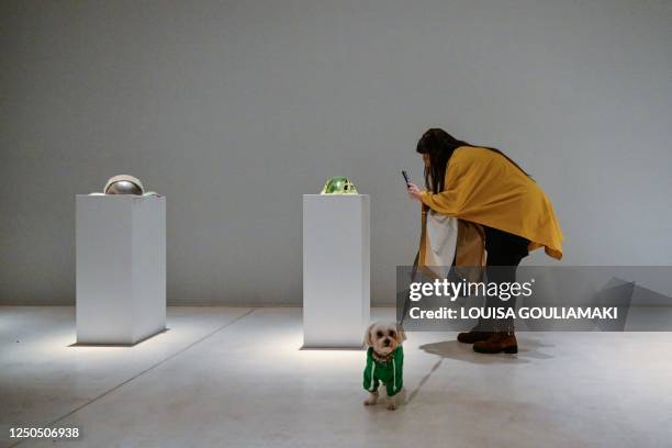 Woman takes a photo as she holds the leash of her dog during a visit to the The National Museum of Contemporary Arts in Athens on April 2, 2023...