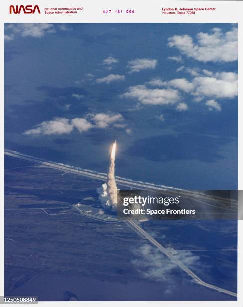 Aerial view of the launch of Space Shuttle Atlantis leaving an exhaust plume, with the orbiter riding atop the glow of the firing solid rocket...