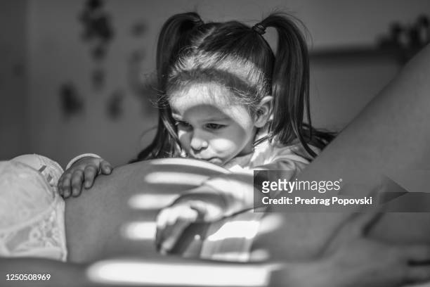 artistic image with blinds light falling over portrait of pregnant mom and her daughter as they expecting a birth of a second child - baby touching belly fotografías e imágenes de stock