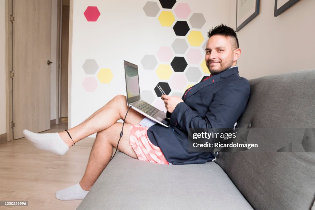 Hombre latino está en casa trabajando vestido con una chaqueta y corbata y en la parte inferior pantalones cortos casuales