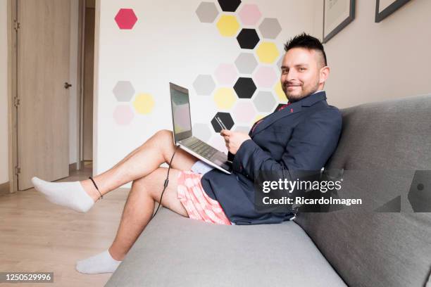 hombre latino está en casa trabajando vestido con una chaqueta y corbata y en la parte inferior pantalones cortos casuales - pantalón corto fotografías e imágenes de stock