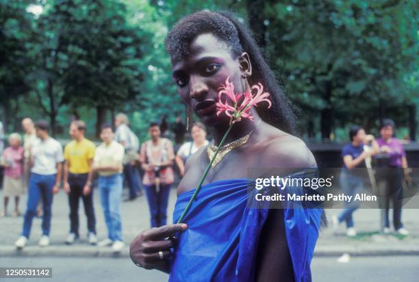 Portrait of an unidentified participant, dressed in a blue wrap and gold necklace, posing with a flower during the New York City March, 1980s or...