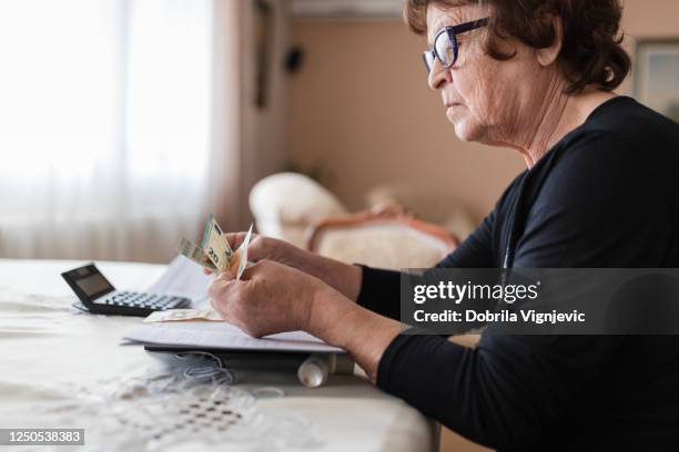 senior woman holding money in her hands at home - starving woman stock pictures, royalty-free photos & images