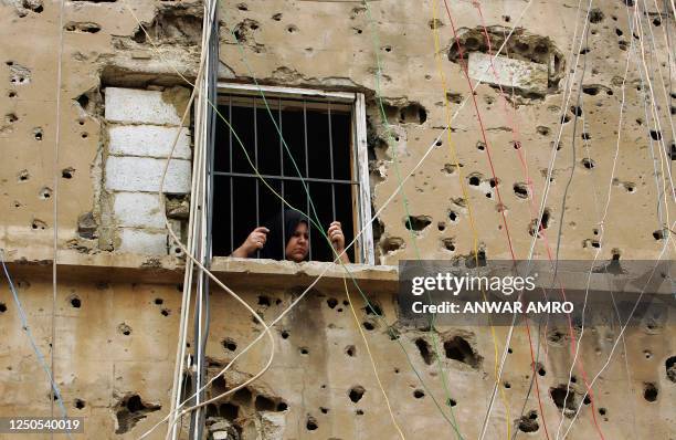 Palestinian woman looks out the window of her bullet pocked home as she watches a rally by women marking International Women's Day at the Burj...