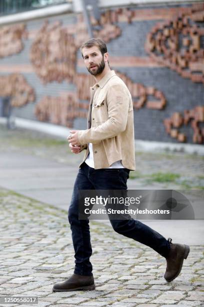 Influencer and model Andre Hamann, wearing a beige shirt by Belstaff, a white t-shirt by Topman, dark blue denim jeans by Calvin Klein, brown boots...