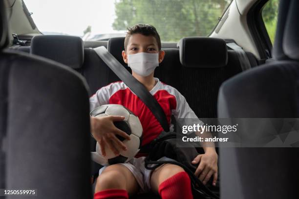 niño en un coche en su camino a la práctica de fútbol usando una máscara facial para evitar la pandemia de coronavirus - football face mask fotografías e imágenes de stock