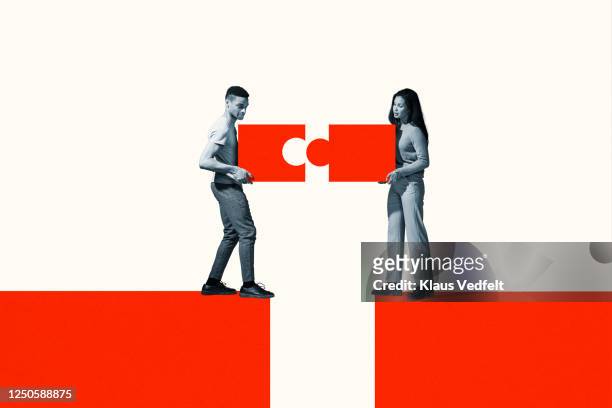 man and woman positioning orange puzzle pieces - positionner photos et images de collection