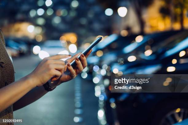 cropped shot of a woman's hand using smartphone while walking to her car in car park in city at night - car shopping stock-fotos und bilder