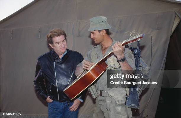 Eddy Mitchell joue de la guitare avec un soldat à son arrivée dans le camp militaire français de Miramar.