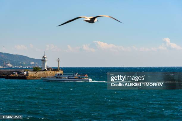 a lighthouse in the port of the resort city of yalta, on a bright sunny day with clouds in the sky, a telescope on the horizon and a flying seagull in the sky. - yalta - fotografias e filmes do acervo